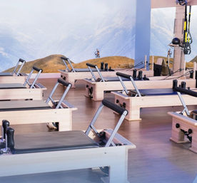 Bright Pilates reformer studio interior with rows of wooden reformer beds on a light hardwood floor and a scenic mountain mural backdrop