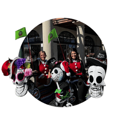 Festive outdoor market stall featuring colorful Day of the Dead–style skull and skeleton decorations with two vendors in red jackets under arched storefronts.