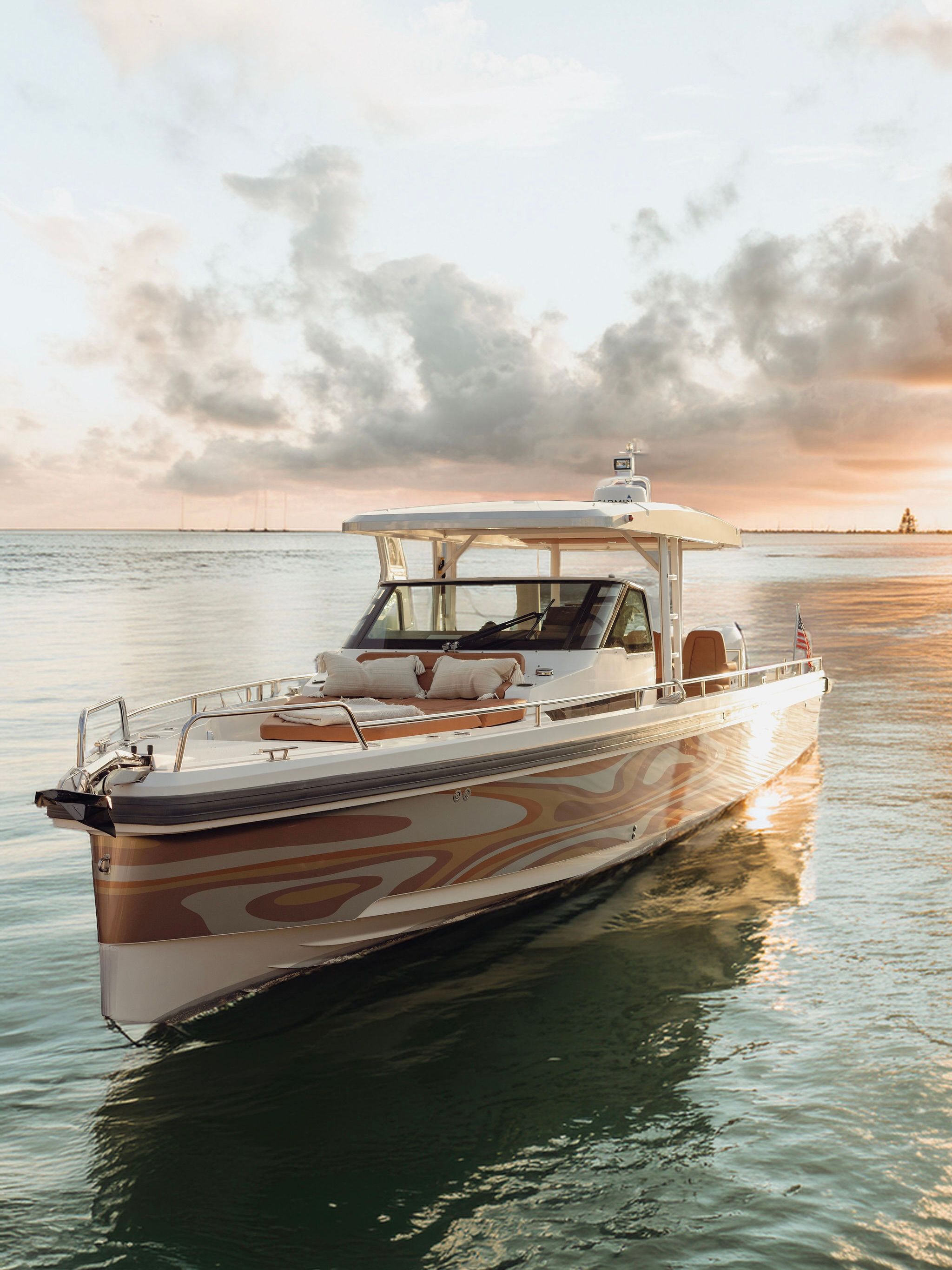 Luxury motorboat with patterned hull and cushioned bow lounge on calm coastal waters at golden sunset