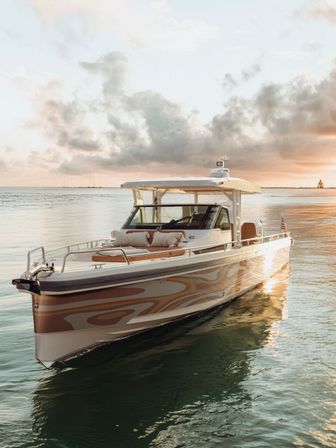 Luxury motorboat with patterned hull and cushioned bow lounge on calm coastal waters at golden sunset
