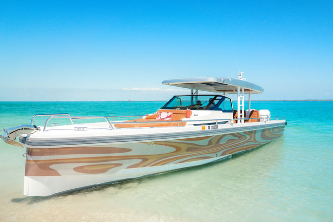 Sleek patterned powerboat anchored on a shallow sandbar in tropical turquoise water under a clear blue sky — sunny coastal day.