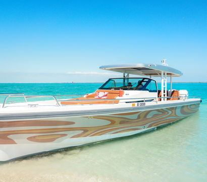 Sleek patterned powerboat anchored on a shallow sandbar in tropical turquoise water under a clear blue sky — sunny coastal day.