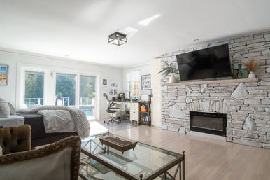 Bright modern living room-bedroom with stacked stone fireplace and wall-mounted TV, glass coffee table, bed and home office by sliding doors to a backyard pool