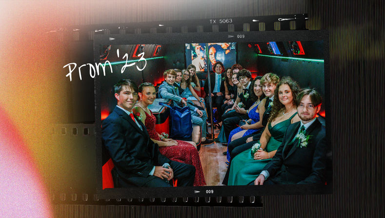 Group of teens in formal dresses and suits seated along both sides of a party-bus interior, smiling and posing for a prom photo under colorful LED lighting and a center pole, with handwritten "Prom '23" overlay.