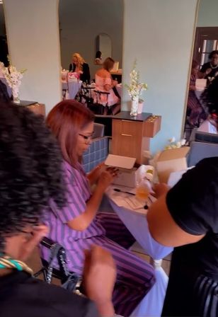 Busy nail salon interior with women enjoying a manicure party at mirrored stations, floral arrangements, manicure boxes and drinks.