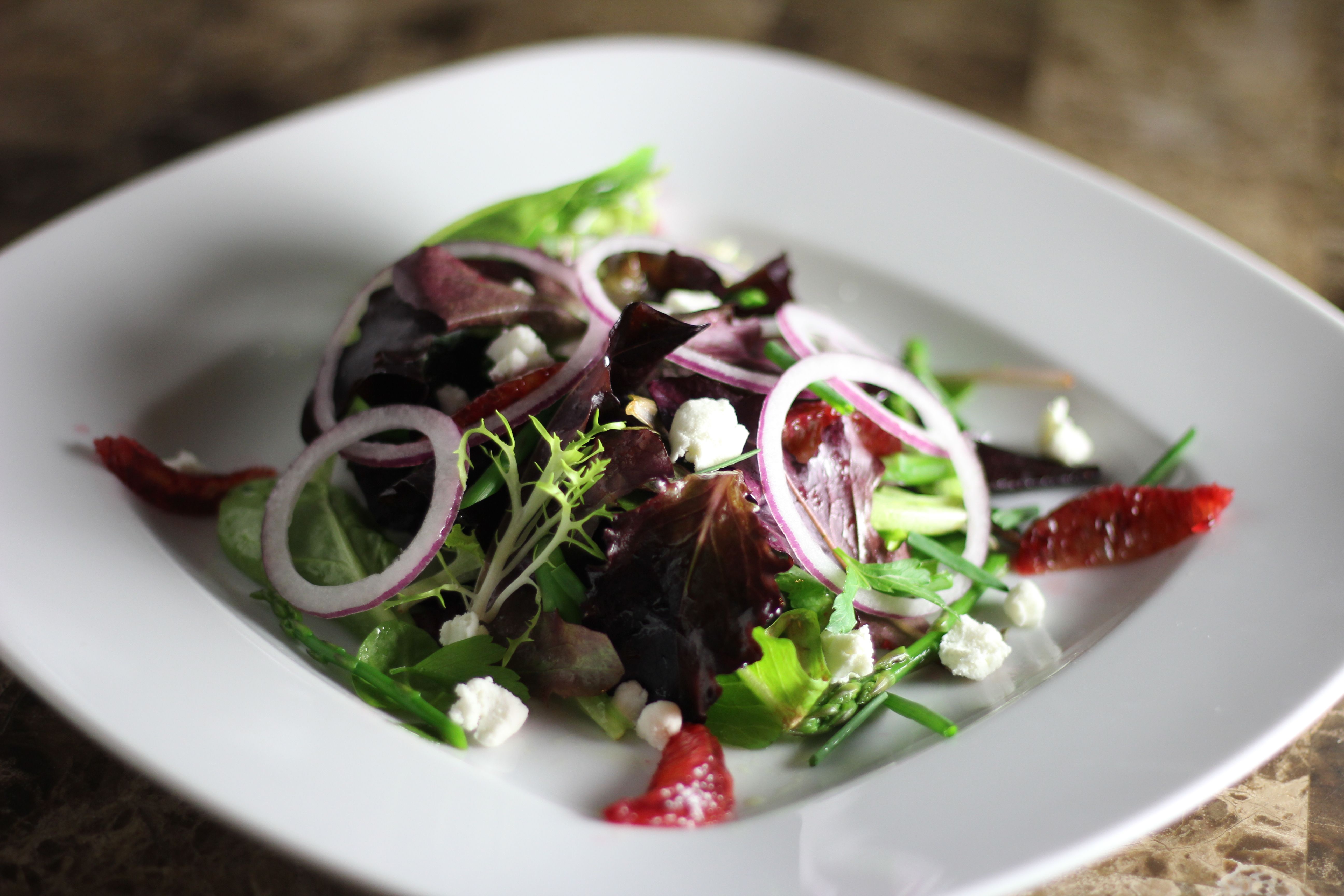 Gourmet mixed greens salad with red onion rings, crumbled goat cheese and blood orange segments on a white plate