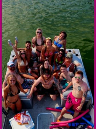 Smiling group of friends partying on a pontoon boat on a sunny lake—swimsuits, sunglasses, drinks and pool noodles as they pose for the camera.