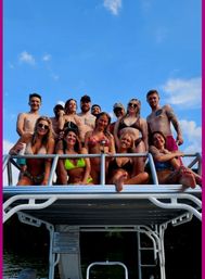 Group of friends in swimsuits posing on the upper deck of a pontoon boat over a lake on a bright blue summer day — smiling, relaxed, enjoying a boat party.