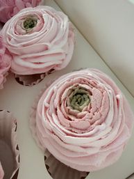 Close-up of pastel pink rose-shaped buttercream cupcakes with swirled frosting in a white bakery box