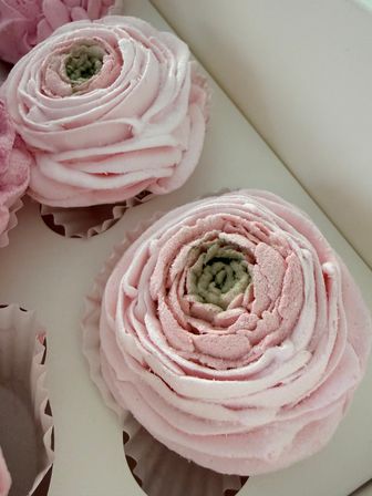 Close-up of pastel pink rose-shaped buttercream cupcakes with swirled frosting in a white bakery box