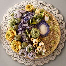 Top-down view of a round buttercream floral cake decorated with pastel piped roses, buds and textured frosting, sitting on a lace paper doily — artisan dessert centerpiece