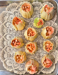 Metal baking tray lined with vintage lace doilies holding a dozen peach-and-cream piped buttercream flower buds, with one pale green bud, arranged in neat rows