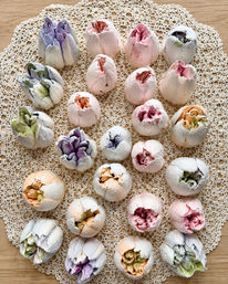 Pastel meringue cookies shaped like peony buds arranged on a crocheted lace doily over a wooden tabletop — colorful shabby‑chic dessert display
