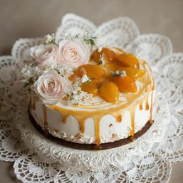 Peach caramel-drip buttercream cake topped with glazed peach halves and blush roses, presented on a vintage lace doily