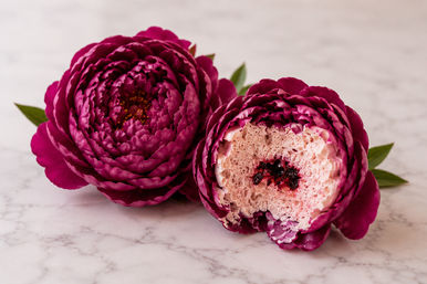 Petal-perfect magenta peony pastries on marble, one sliced to reveal airy pink sponge mousse and jammy dark-berry center with green leaves