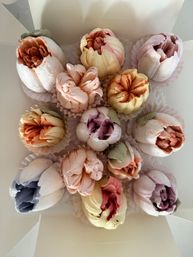 Box of pastel flower-shaped meringue cookies — assorted pink, peach, yellow and lavender peony-style confections in white paper cups