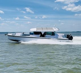 Sleek white cabin motorboat cruising across calm coastal waters with a foamy wake under a sunny blue sky — summer boating on the bay.