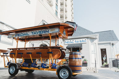 Bright yellow multi-seat pedal bar parked outside a downtown Nashville tavern, with a wooden barrel and white brick building in the background.