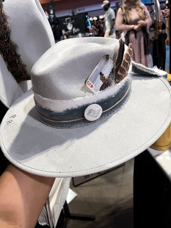 Light gray felt fedora with denim hatband, feather and Queen of Hearts playing card tucked into the band, displayed at an indoor market booth.