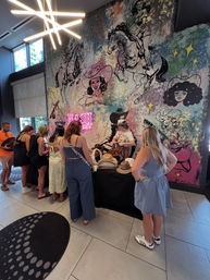 People browsing a cowboy hat pop-up inside a venue in front of a colorful Nashville-inspired mural of cowgirls, horses and neon accents