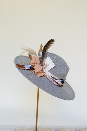Gray felt wide-brim fedora on a gold stand, styled with a patterned silk scarf band, peach bow, decorative feathers and a vintage playing card — women's fashion hat display