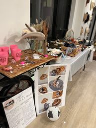 Indoor boho hat bar for a bridal party — cowboy and felt hats on stands, wooden crates of ribbons, feathers and trims, dried floral vase, pink 'Bride’s Last Ride' cups, styling poster and accessories on a wooden table.
