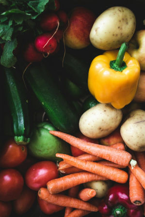Close-up of garden-fresh produce: yellow bell pepper, baby potatoes, carrots, radishes, cucumbers and tomatoes — vibrant fresh vegetables
