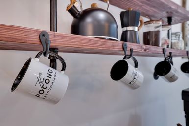 Cozy modern farmhouse kitchen shelf with white enamel coffee mugs hanging on hooks, black kettle and stovetop espresso maker on a rustic wooden plank