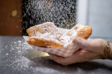 New Orleans-style beignets dusted with powdered sugar falling into a checkered paper tray held in hands