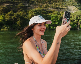 Smiling young woman in a cap taking a selfie on a boat on a green river with a wooded shoreline