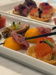 Close-up of gourmet appetizer platter with seared scallop tartlets, prosciutto-wrapped cantaloupe balls, and sesame-crusted tuna on a white serving tray