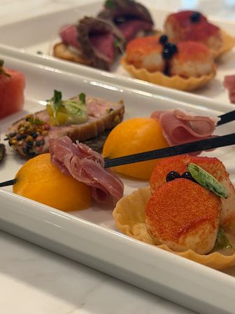 Close-up of gourmet appetizer platter with seared scallop tartlets, prosciutto-wrapped cantaloupe balls, and sesame-crusted tuna on a white serving tray