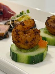 Close-up of a spicy grilled shrimp canapé on a cucumber round topped with avocado mash and bright orange salmon roe, plated as a gourmet seafood appetizer.