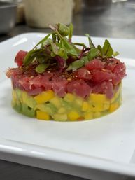 Gourmet ahi tuna tartare tower with diced mango and avocado, topped with microgreens and seasoning on a white plate