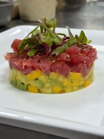 Gourmet ahi tuna tartare tower with diced mango and avocado, topped with microgreens and seasoning on a white plate