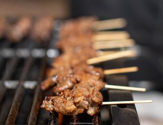 Close-up of juicy marinated beef skewers sizzling on a BBQ grill, bamboo sticks lined up on metal grates with a blurred background