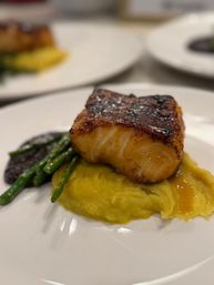 Seared caramelized white fish fillet atop creamy mashed sweet potato with sautéed asparagus and a dark sauce, restaurant-style on a white plate