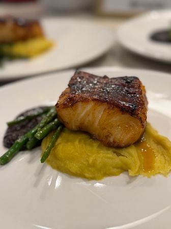 Seared caramelized white fish fillet atop creamy mashed sweet potato with sautéed asparagus and a dark sauce, restaurant-style on a white plate