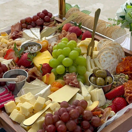 Vibrant charcuterie board close-up with assorted cheeses, cured meats, green and red grapes, strawberries, crackers, olives, nuts and a honey dipper — stylish party grazing board.