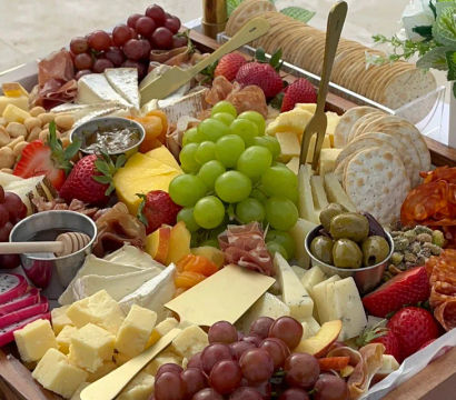 Vibrant charcuterie board close-up with assorted cheeses, cured meats, green and red grapes, strawberries, crackers, olives, nuts and a honey dipper — stylish party grazing board.