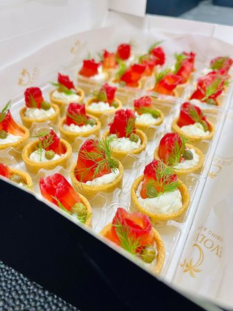 Tray of bite-sized smoked salmon tartlets - mini pastry cups filled with herbed cream cheese, smoked salmon rosettes, capers and fresh dill, arranged as elegant catering appetizers.