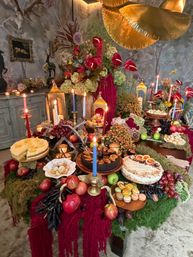 Opulent autumn tablescape in a moody vintage room: moss-draped table topped with lit tapers and lanterns, lush floral centerpiece, cakes, macarons, apples, grapes and assorted pastries.
