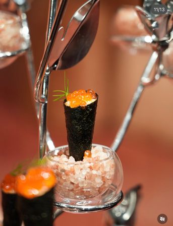 Mini nori cone sushi topped with glossy salmon roe (ikura) and a dill sprig, served upright in a glass of pink rock salt — elegant Japanese appetizer