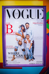 Playful poster of a smiling family striking illusion poses—one parent holding a child upside-down—inside a purple-framed display promoting a Los Angeles museum photo‑op and family attraction.