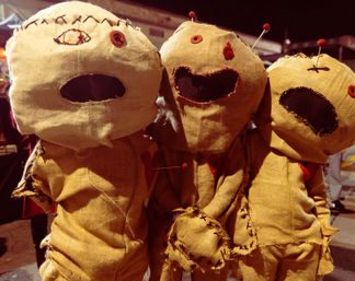Three burlap voodoo-style dolls with stitched faces, button eyes and pins in their heads, posed together in a nighttime outdoor Halloween display.
