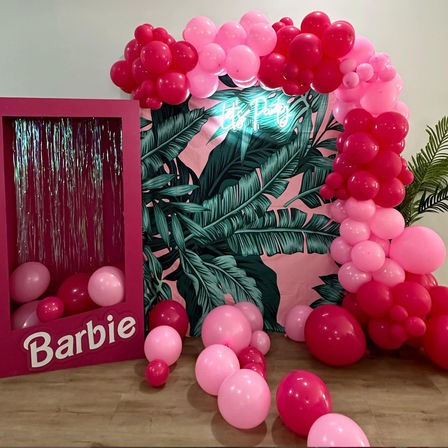 Barbie-themed pink photo booth with tropical leaf backdrop, neon "Let's Party" sign and pink balloon arch for a birthday party