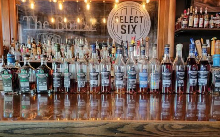 Polished wooden bar with a neat row of whiskey bottles and taps, warm hanging lights and mirrored shelves creating bright reflections.