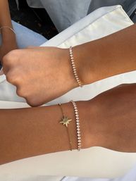 Close-up of two wrists wearing stacked sparkling diamond tennis bracelets and a delicate gold star charm bracelet resting on white linen, layered bracelet jewelry.