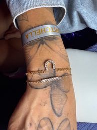 Close-up of a wrist wearing layered gold chain and crystal bracelets over butterfly tattoos — stylish fashion accessory shot.