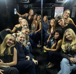Cheerful group of women inside a party bus gathered around a center pole, holding drinks and enjoying a girls' night out nightlife ride.